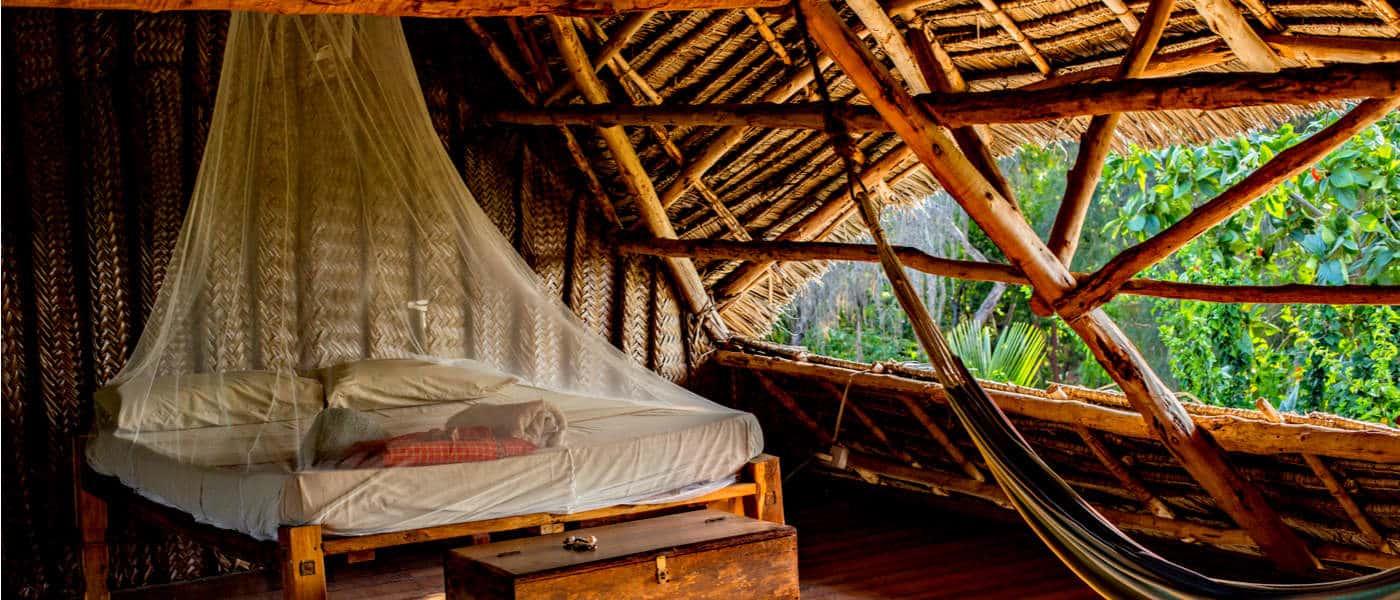 Bed covered by a mosquito net and hammock in a hut