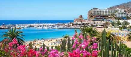 View of Puerto Rico's beach with pink flowers in front. Gran Canaria, Canary Islands, Spain