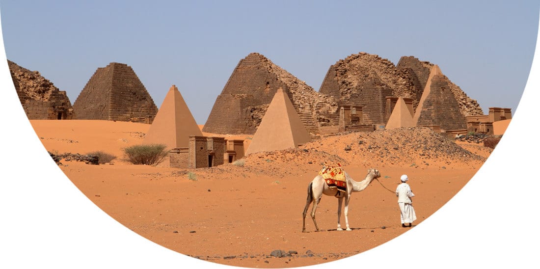 Man holding camel next to pyramids in Sudan